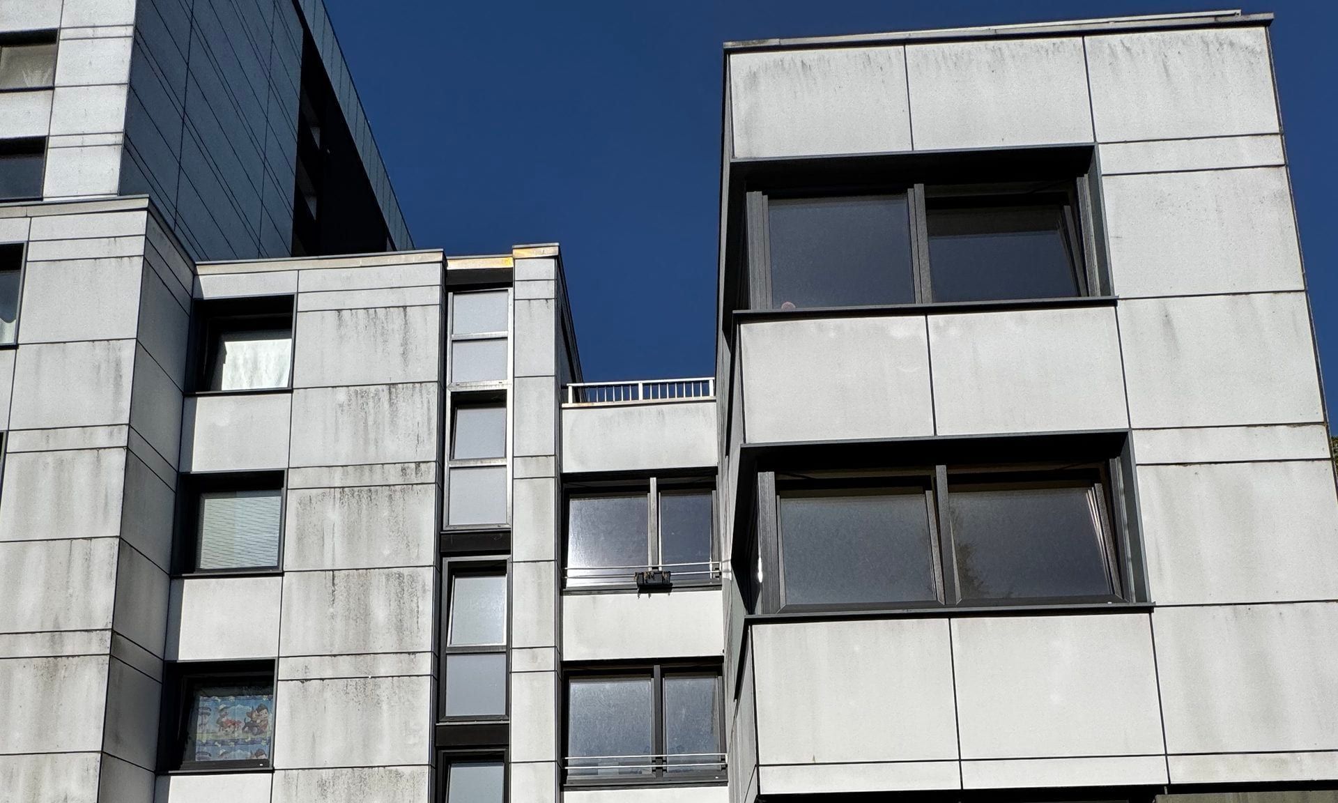 Helle Fassade des dreigeschossigen Hauses, links dahinter das Hochhaus