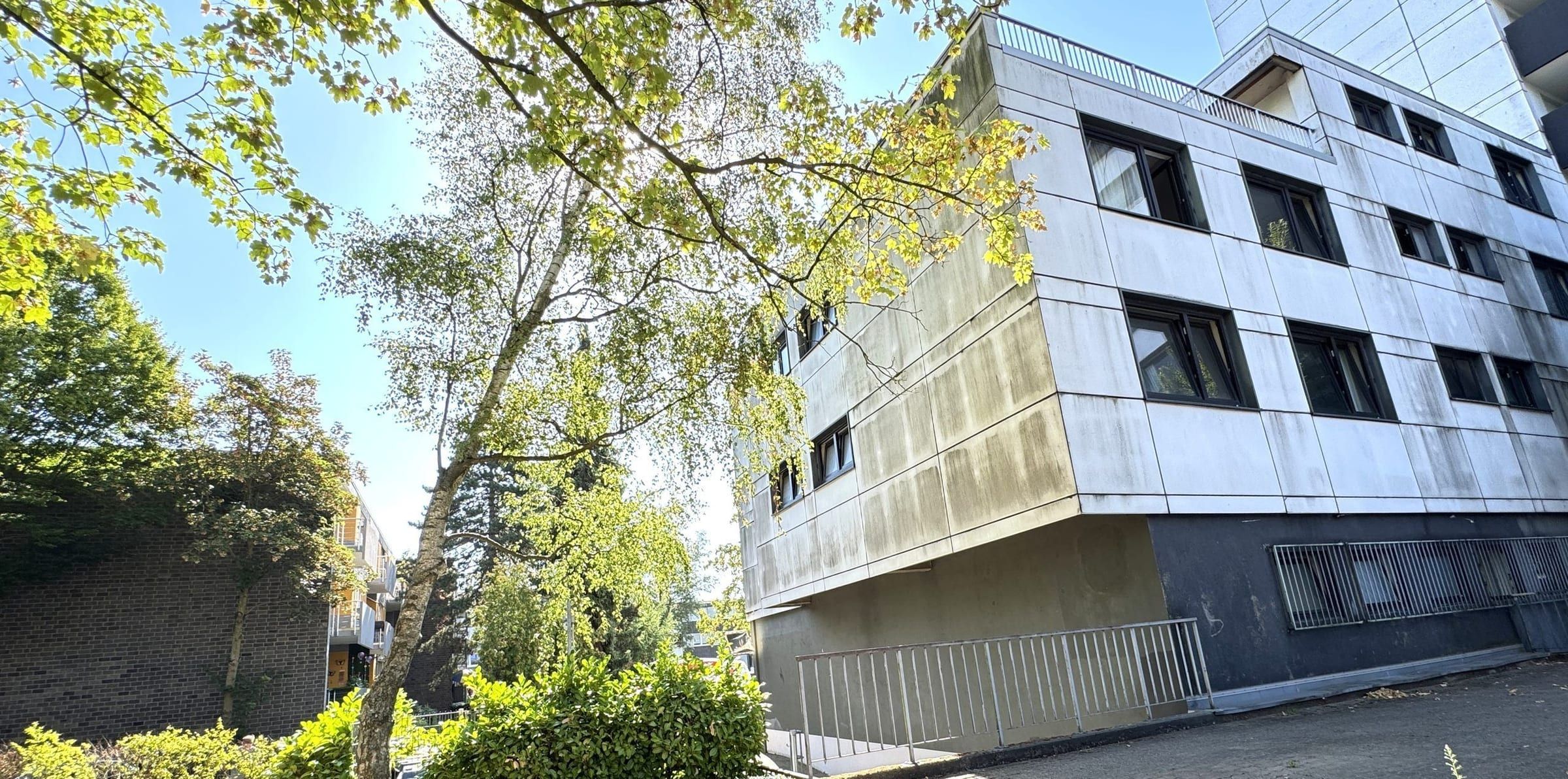Helles dreigeschossiges Haus hinter Bäumen